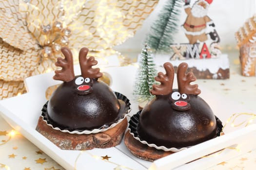 Two chocolate deer cakes in a white wooden tray on a table with christmas decoration, close-up side view.