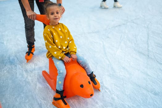 Child glides across ice rink on toy. Child glides across ice rink. Family socializing in winter, playing sports and having fun in snow. Daughter enjoying winter activities