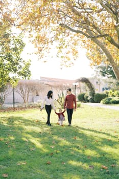 Mom and dad are walking in the park holding the hands of a little girl. High quality photo