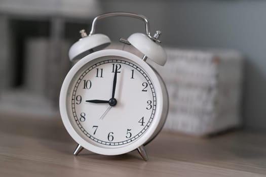 Close-up of a round white alarm clock on a table in the bedroom. The hands on the clock show nine o'clock in the morning, time to get up. Retro alarm clock on the table, vintage tone. space for text