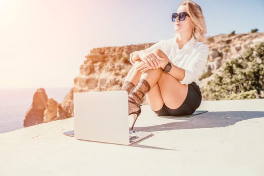 Happy girl doing yoga with laptop working at the beach. beautiful and calm business woman sitting with a laptop in a summer cafe in the lotus position meditating and relaxing. freelance girl remote work beach paradise