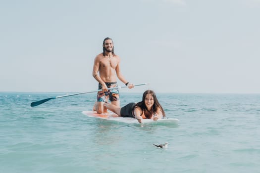 Sea woman and man on sup. Silhouette of happy young woman and man, surfing on SUP board, confident paddling through water surface. Idyllic sunset. Active lifestyle at sea or river