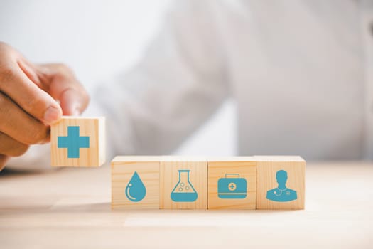 Hand holds wooden block featuring healthcare and medical icons, conveying safety, health, and family well-being. Signifying pharmacy, heart care, and happiness. health care concept