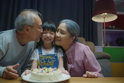 Happy Birthday. Asian family grandfather and grandmother kissed granddaughter feeling thankful while celebrating his birthday after giving wonderful cake, senior family party with child at home