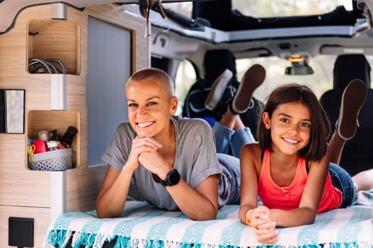 mother and daughter relaxing lying in the back of their camper van, concept of active tourism in nature and outdoor activities with children