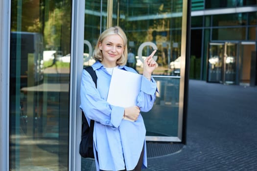 Image of young college girl, young woman with laptop, posing near university building, standing on street, smiling, concept of education and people.