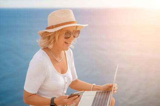 Freelance women sea working on the computer. Good looking middle aged woman typing on a laptop keyboard outdoors with a beautiful sea view. The concept of remote work