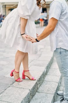 Woman leaned towards man holding her hands while standing on the steps. Cropped. Faceless. High quality photo