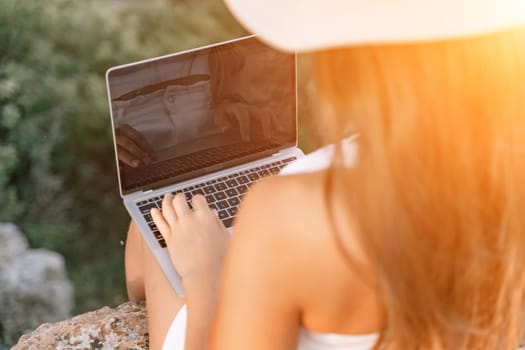 Freelance women sea working on the computer. Good looking middle aged woman typing on a laptop keyboard outdoors with a beautiful sea view. The concept of remote work