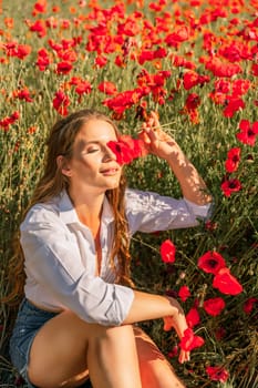 Woman poppies field. Happy woman is resting in the rays of the sun sitting in the poppy field