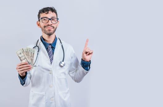 Handsome smiling doctor showing money and pointing side. Happy young doctor holding money and pointing to side. Latin doctor