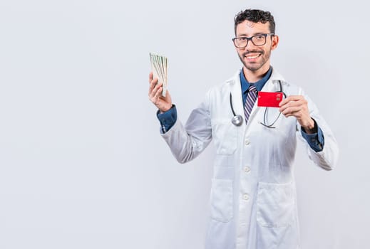 Happy young doctor holding credit card and money isolated. Handsome doctor holding money and credit cards isolated