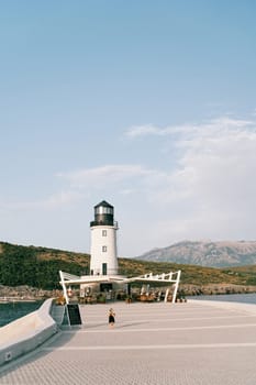 Little girl walks along the pier against the backdrop of a lighthouse with an outdoor restaurant. High quality photo
