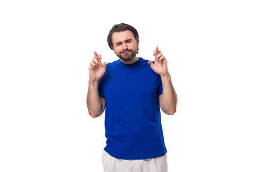 young handsome european man with black hair and beard dressed casually crossed his fingers and hopes against the background with copy space.