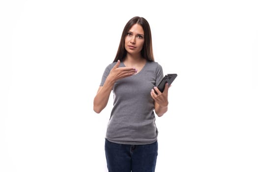 young european brunette woman dressed in a gray t-shirt uses a smartphone in her hand.
