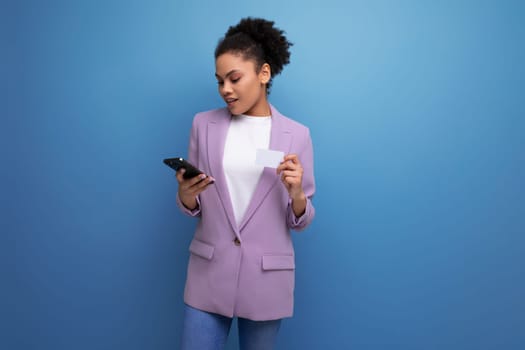 young successful positive office woman dressed in a jacket pays for purchases using a smartphone and a credit card.