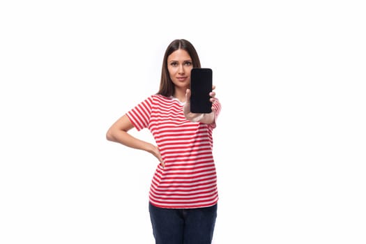 young brunette woman in a red red-white striped t-shirt holding a smartphone with a mockup for advertising on a white background with copy space.