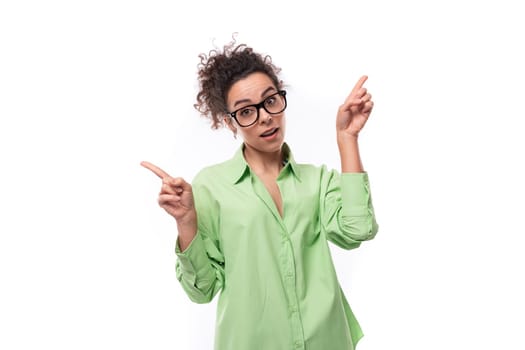 pretty young brunette curly woman in glasses is dressed in a green shirt on a white background with copy space.