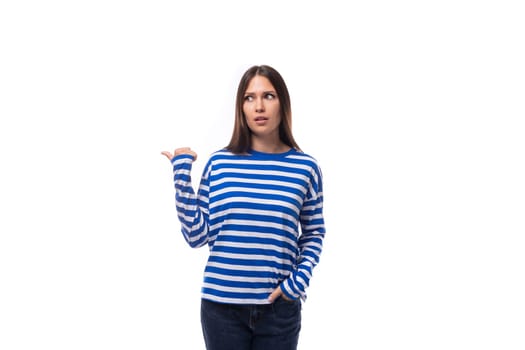 young caucasian woman with dark hair dressed in a blue striped sweatshirt points her hand to the side on a white background.