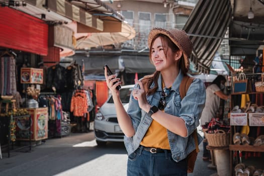 Young Asian tourist walking along city streets and holds a mobile phone on the pavement.