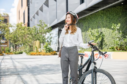 Asian young businesswoman putting biking helmet prepared cyclists around building go to work, Close up smiling woman wearing helmet exercise outdoors with bicycle on street, Transport Save Energy