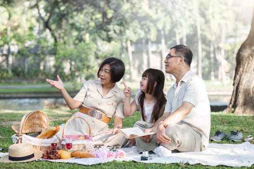 Family of senior couple and daughter picnicking in the park showing love Or reconnect after retirement in a relaxing park. An elderly man and a woman have fun on a mat in the backyard..