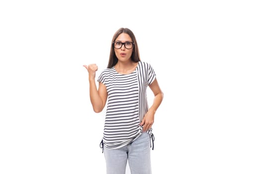 young pretty caucasian brunette woman in a striped t-shirt points her hand to the side on a white background with copy space.
