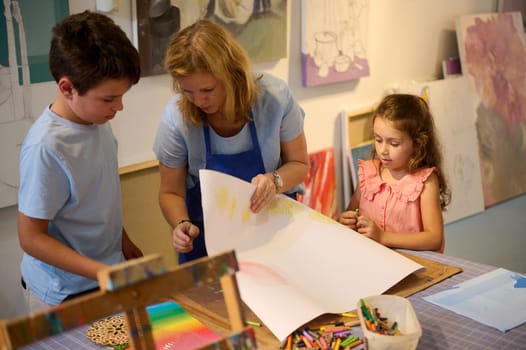 Creative diverse kids during art class in elementary school classroom drawing with female teacher. Learning painting. People. Fine art. Education. Developing skills and imagination during art class