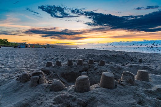 Circle sandcastle in front of beautiful dark golden sunset at golden hour at the beach next to dark and cold sea at summer right after the storm and rain