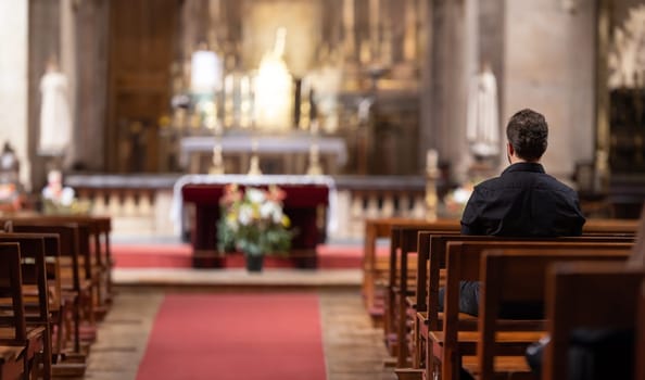 A man sitting in a catholic church looking at the alter