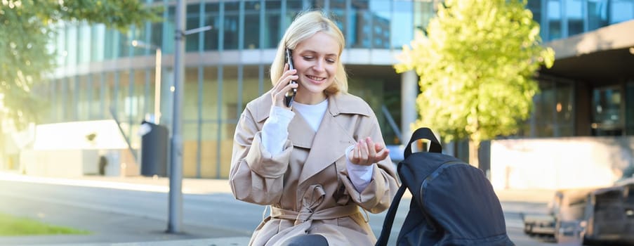 Portrait of young woman sitting on bench, talking on mobile phone, spending time outside, answers a telephone call, having friendly conversation on cellphone.