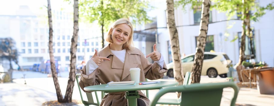Happy smiling cafe client, woman pointing fingers at takeaway coffee, recommending restaurant, outdoor space on street, giving positive feedback, recommending place.