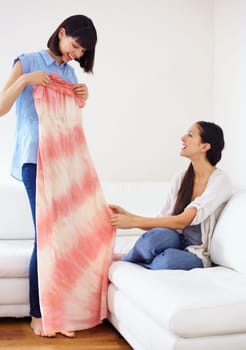 Woman, friend and showing of dress in home for opinion, decision and choice of clothes. Happy people, smiling and excitement for gift with cool, trendy or casual fashion for summer in living room.