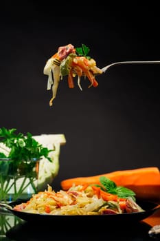 cooked fried cabbage with vegetables and sausages, on a fork isolated on a black background