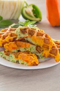 cooked two-color vegetable waffles made from cabbage and carrots, in a plate on a wooden table.