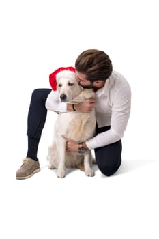 Handsome young man with labrador white dog wearing Santa Claus red hat for Christmas to celebrate the season, on white background in studio