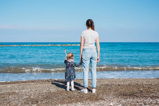 Back view of mother and her little daughter looking at the sea