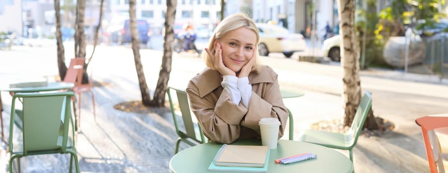 Portrait of cute young woman, student revising for exam in cafe, drinking coffee and studying, doing homework.