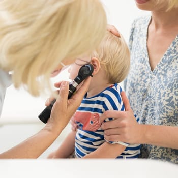 Infant baby boy child being examined by his pediatrician doctor during a standard medical checkup in presence and comfort of his mother. National public health and childs care care koncept