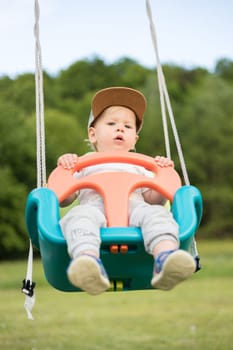 Adorable little happy Caucasian infant baby boy child swinging on playground outdoors