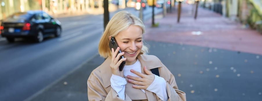 Close up portrait of smiling, happy and carefree woman on streets of big city, laughing while talking on mobile phone, chatting on smartphone and walking. Lifestyle concept