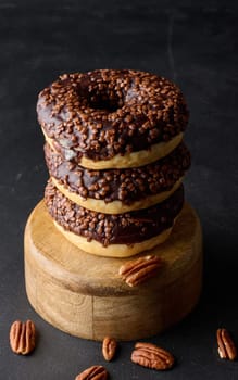 Chocolate donuts sprinkled with crushed nuts on a black table