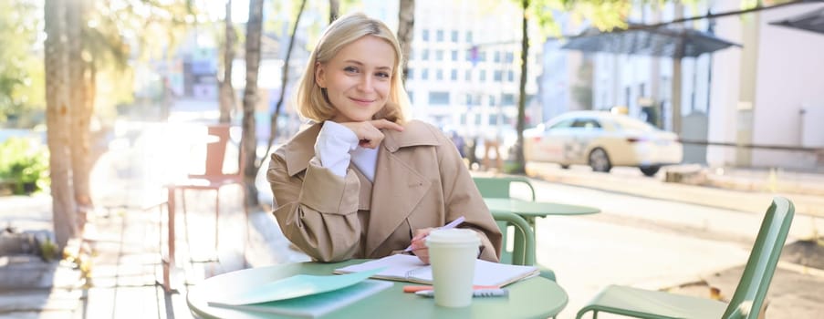 Portrait of cute young woman, student revising for exam in cafe, drinking coffee and studying, doing homework.