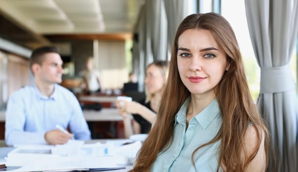 Beautiful smiling cheerful girl at cafe look in camera with colleagues group in background. White collar worker at workspace job offer modern lifestyle client visit profession train concept