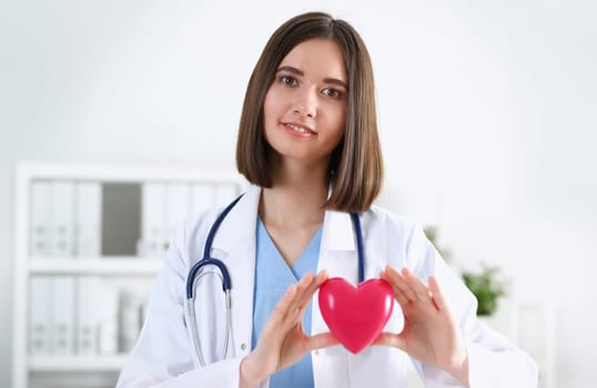 Female medicine doctor hands holding and covering red toy heart closeup. Cardio therapeutist student education physician make cardiac physical heart rate measure arrhythmia concept