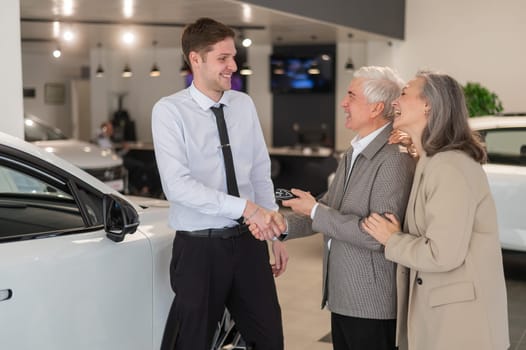 A salesman demonstrates a car with an open hood to an elderly Caucasian couple in a car dealership