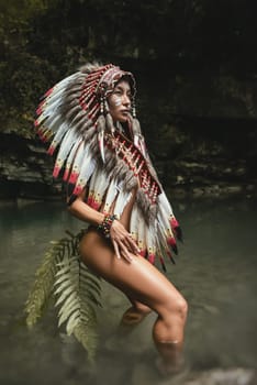Naked girl in Native American headdresses poses sexually against the backdrop of wildlife with a fern