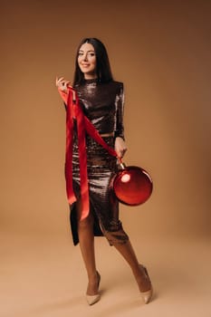 Girl with long hair in a shiny dress with a large Christmas ball on a brown background.