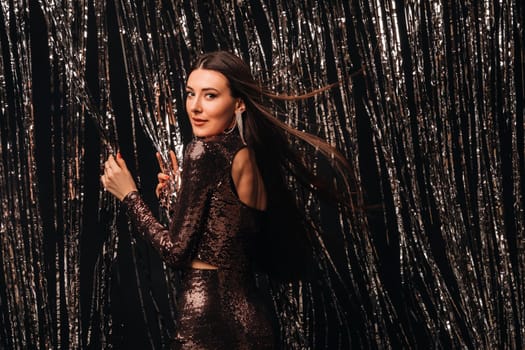 girl in a shiny dress on a silver background of New Year's rain with developing hair.