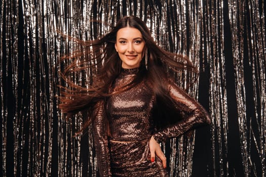 girl in a shiny dress on a silver background of New Year's rain with developing hair.